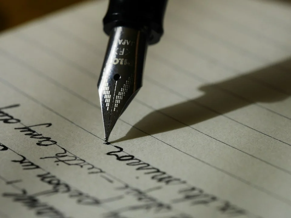 A close-up of a fountain pen writing on paper in warm directional light.