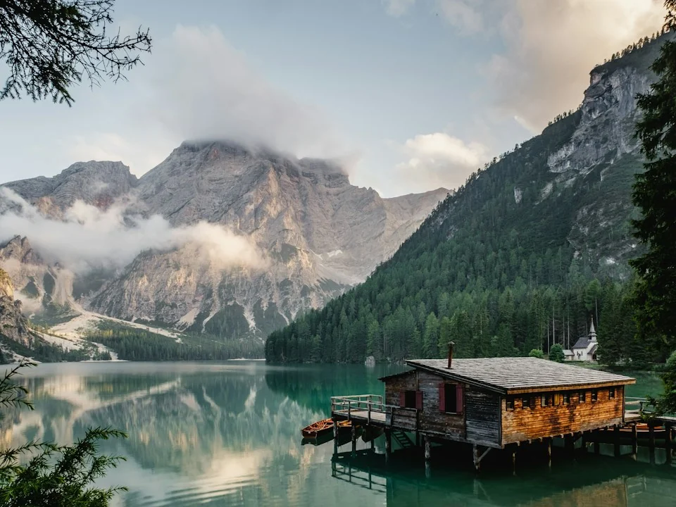 An alpine lake and wooden boathouse framed by mountains and drifting clouds.